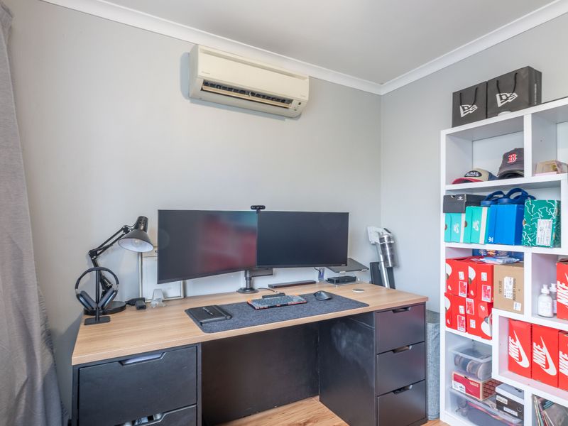 A functional home office space featuring a wall-mounted split-system air conditioner, neutral wall finishes, and laminate flooring.