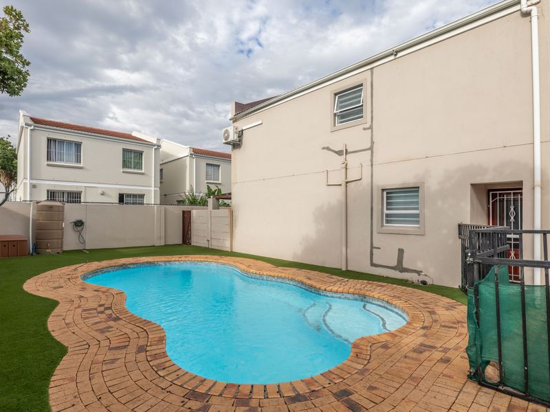 A private backyard area featuring a swimming pool with brick paving, artificial turf, and perimeter walling in a townhouse complex setting.