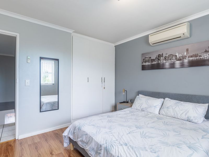 A well-maintained bedroom featuring laminate flooring, built-in cupboards, and a wall-mounted split-system air conditioner.