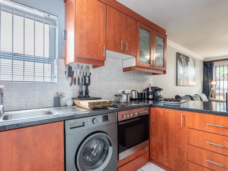 Open-plan kitchen featuring warm-toned wooden cabinetry, granite countertops, integrated appliances, and a tiled backsplash, flowing seamlessly into the adjacent living area.