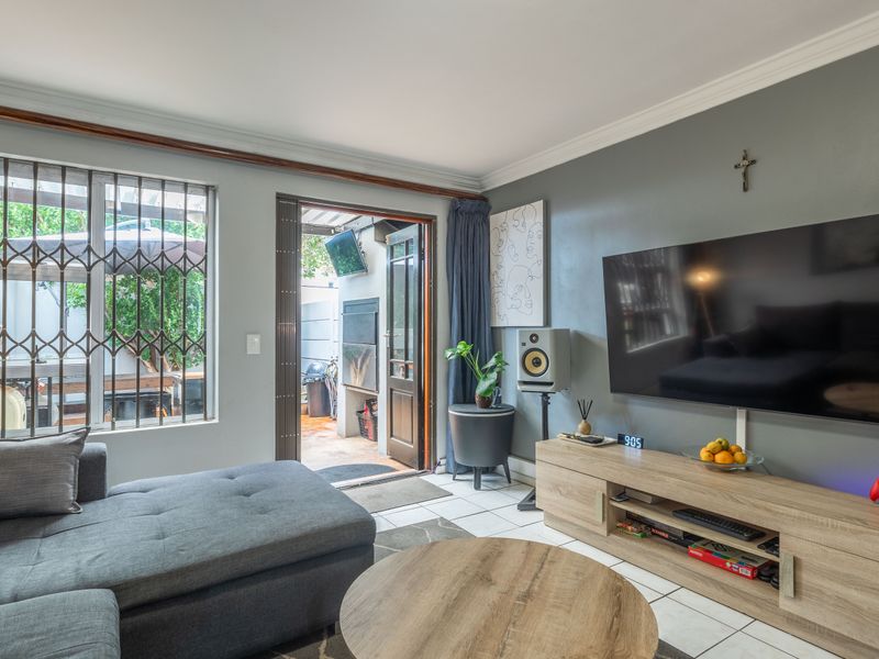 A comfortable living room featuring tiled flooring, decorative cornicing, and direct access to an outdoor patio area through a glass door.