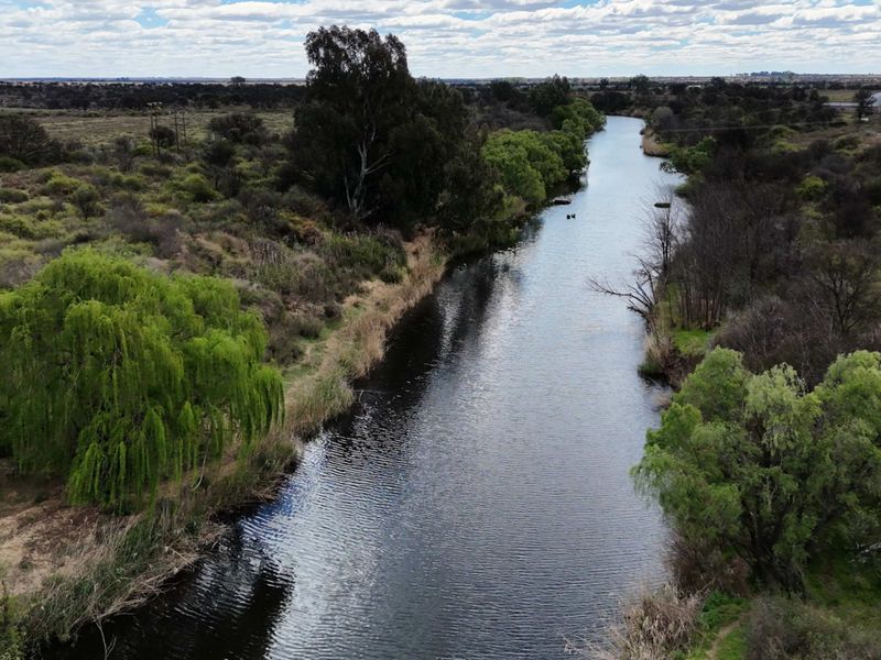 An aerial view of a natural river flowing through the farm landscape, surrounded by mature trees and indigenous vegetation.