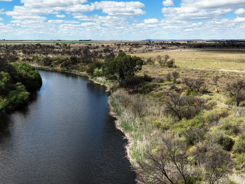 An aerial view of a natural river flowing through the expansive rural landscape of the farm property.