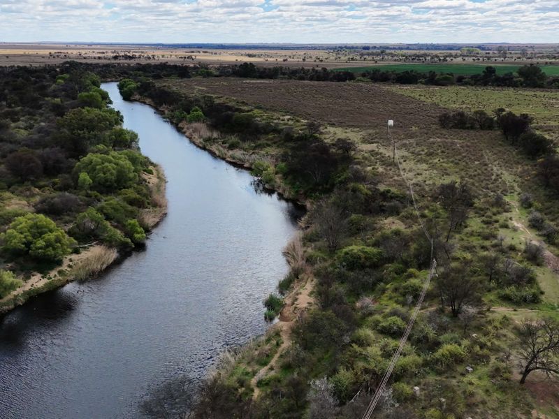 An aerial view of the farm property featuring a river running through the landscape, natural vegetation, and utility infrastructure.