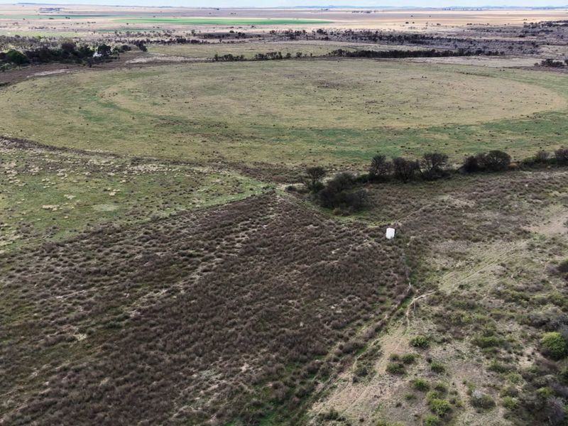An aerial view of the expansive farm landscape, featuring open grazing fields, natural vegetation, and a small water storage tank.