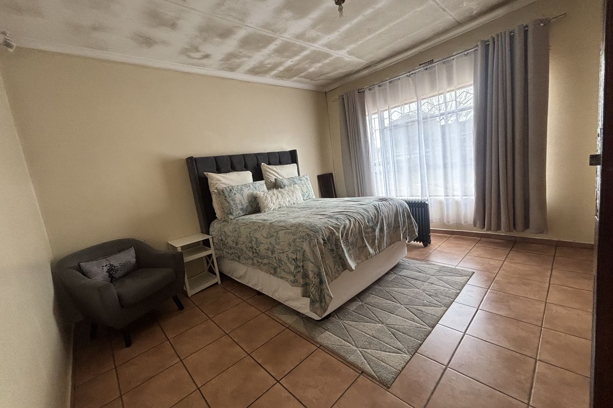 A bedroom featuring tiled flooring and security bars on the window, currently showing signs of ceiling damage requiring maintenance.