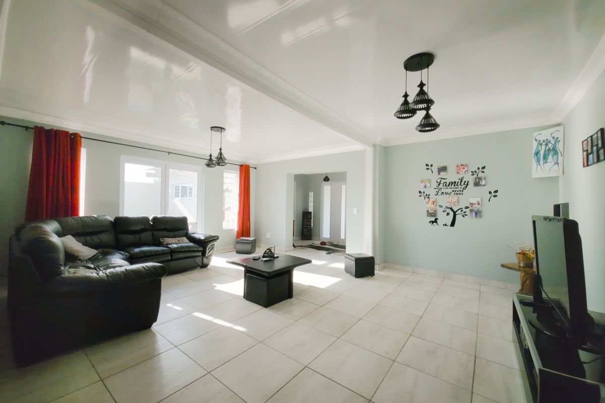 Spacious living room featuring light-colored floor tiles, a high-gloss ceiling finish, and natural light streaming through sliding glass doors.