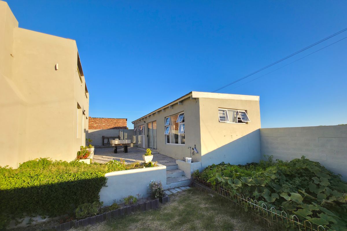 Rear view of the property featuring a paved patio area, landscaped garden beds, and a boundary wall.