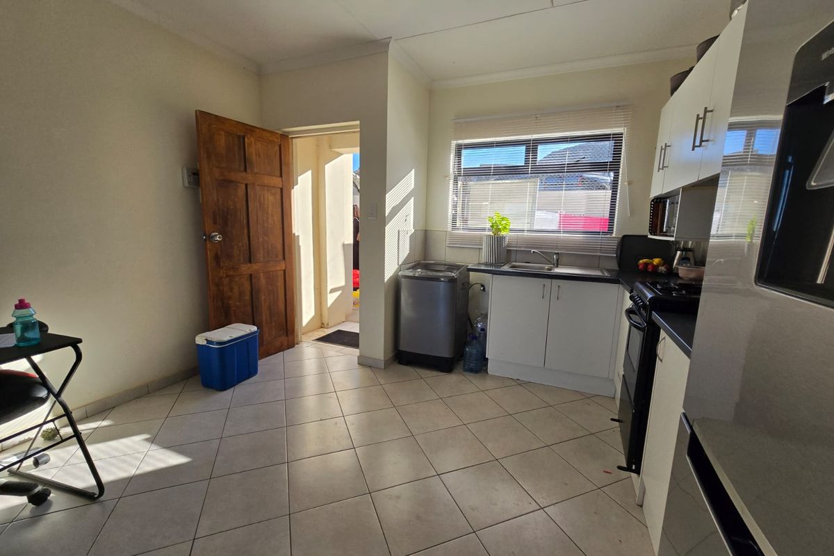 Functional kitchen featuring tiled flooring, built-in cabinetry, a stainless steel sink, and a freestanding stove with direct access to an exterior doorway.