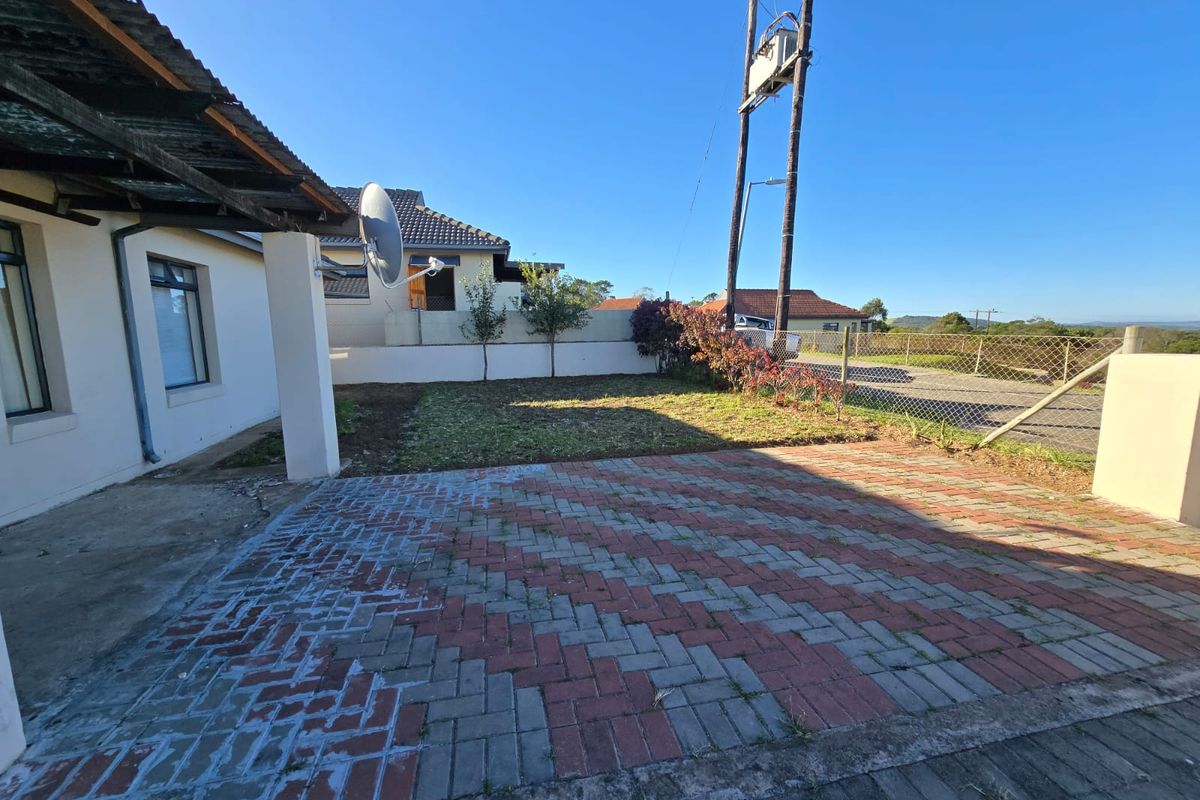Rear exterior view featuring a paved driveway area, covered patio section, and perimeter fencing with a retaining wall.