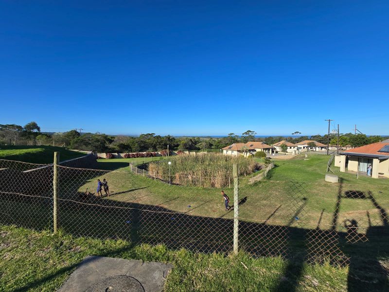 An elevated view overlooking a landscaped pond, surrounding green space, and residential buildings under a clear blue sky.