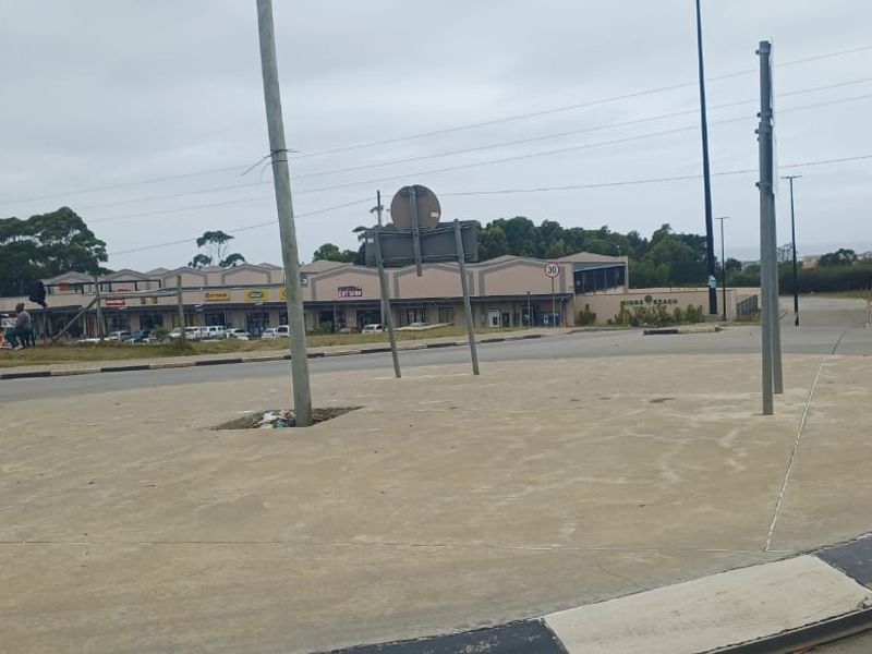 A view of a paved traffic circle and surrounding road infrastructure with commercial buildings in the background.