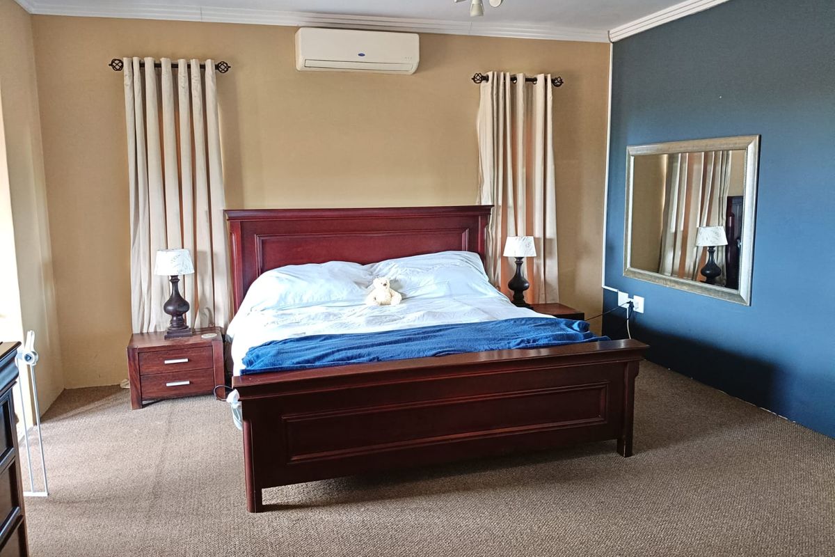 A spacious bedroom featuring carpeted flooring, a ceiling fan, and a wall-mounted split-system air conditioner.