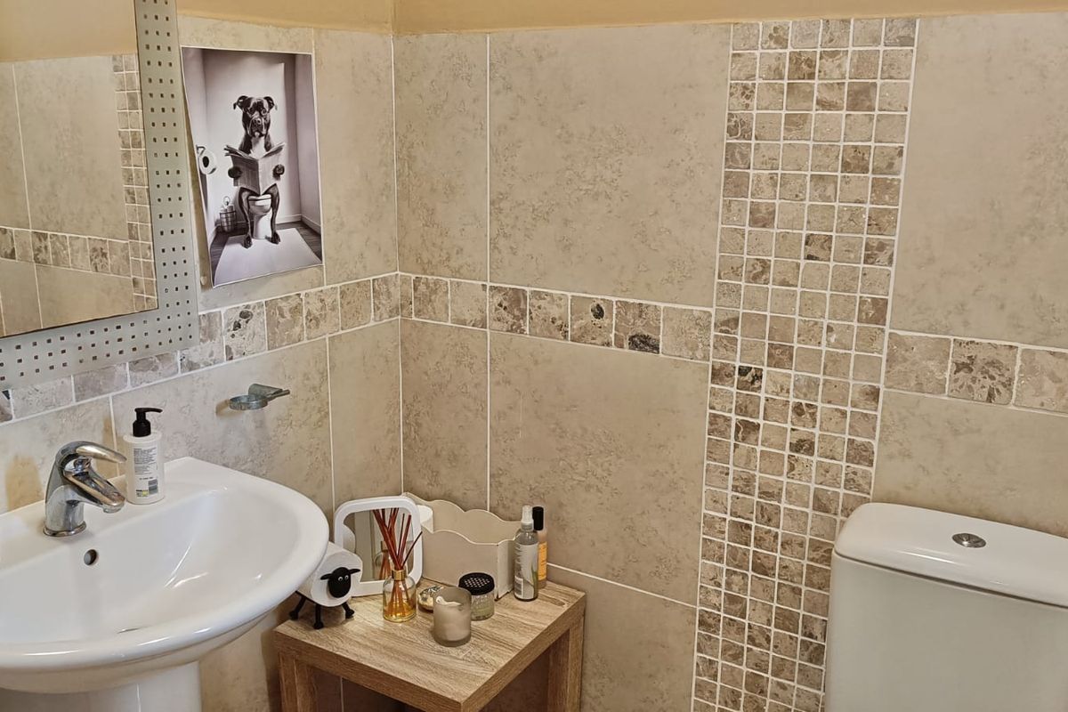 A compact bathroom featuring neutral ceramic wall tiles with a decorative mosaic border, a pedestal basin with chrome mixer tap, and a standard toilet.