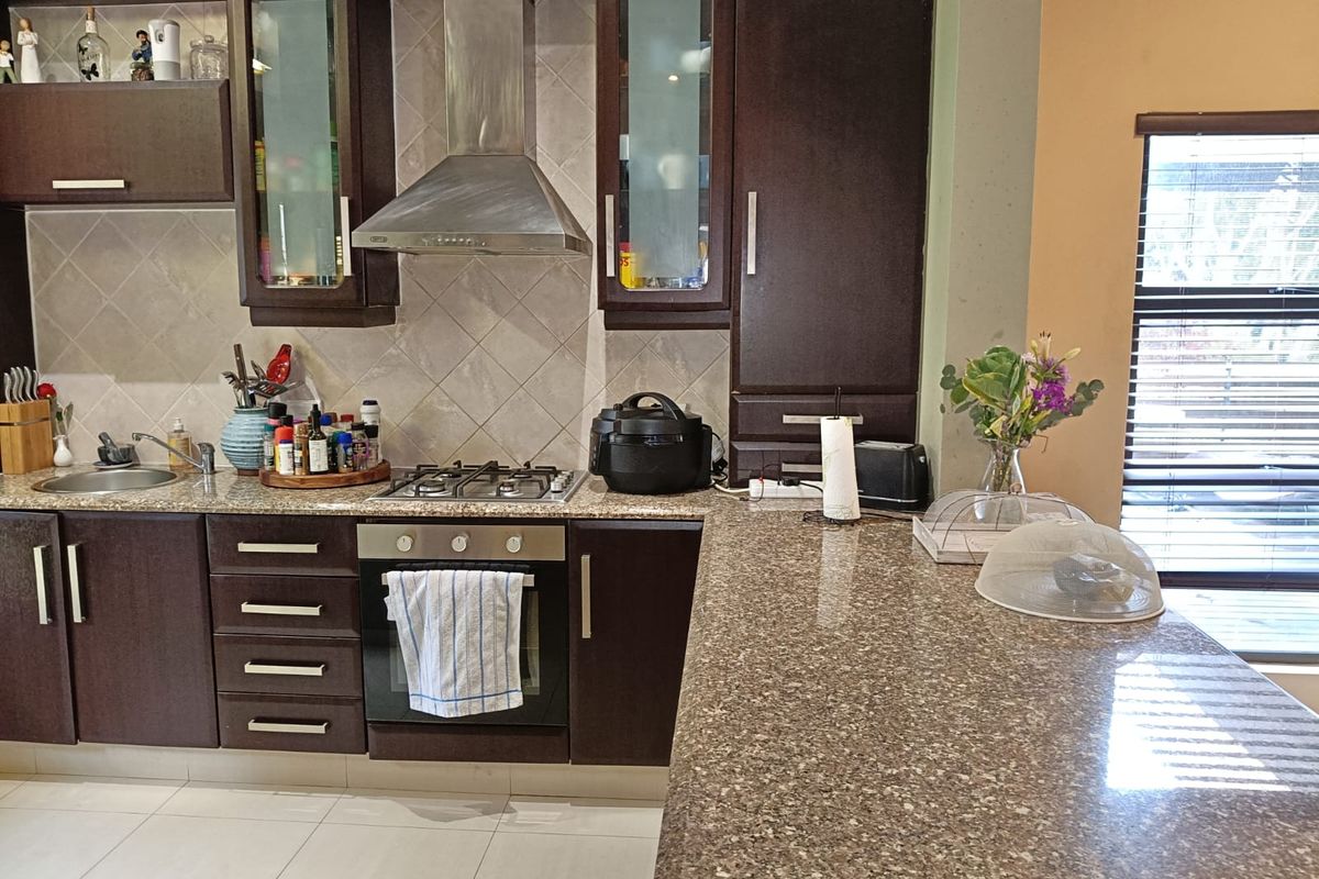 A functional kitchen featuring dark wood cabinetry, granite countertops, a gas hob, built-in oven, and a stainless steel extractor fan with tiled backsplash.