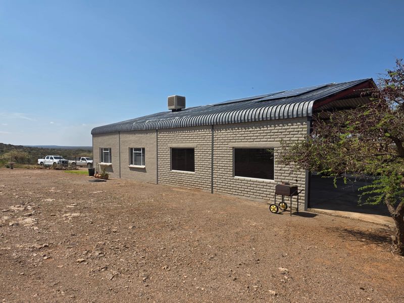 Rear view of a farm building featuring a corrugated metal roof with integrated solar panels, brick masonry walls, and tinted windows.