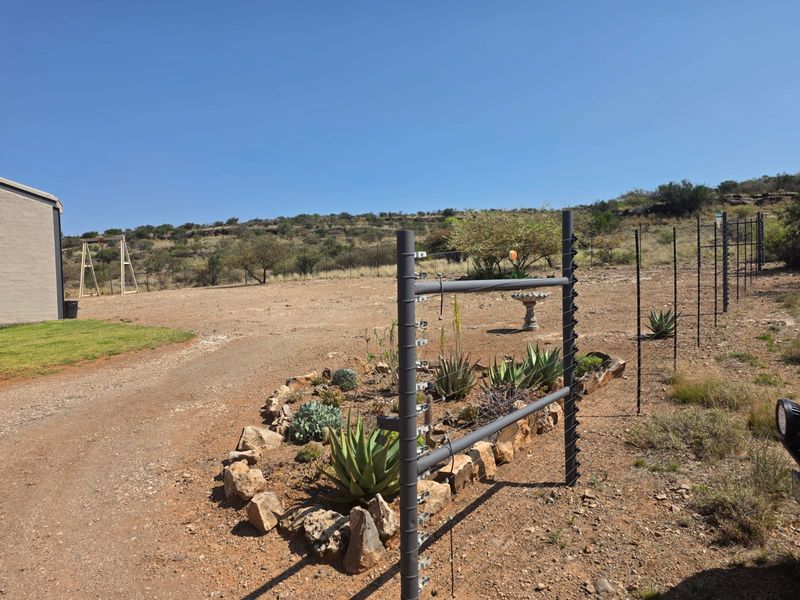 A spacious outdoor area on a farm property featuring a gravel driveway, a rock-bordered garden bed, and secure electric perimeter fencing.