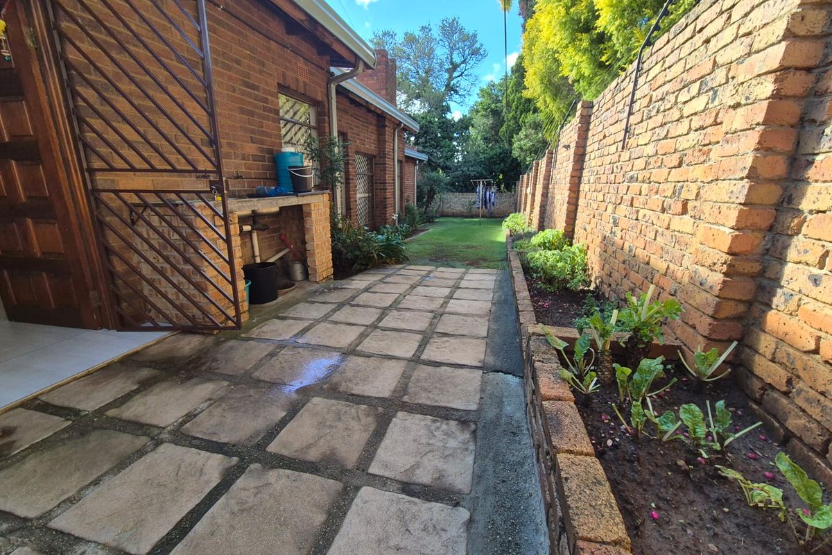 A side exterior view featuring a paved walkway, brick boundary wall, raised garden beds, and a built-in outdoor utility sink area.
