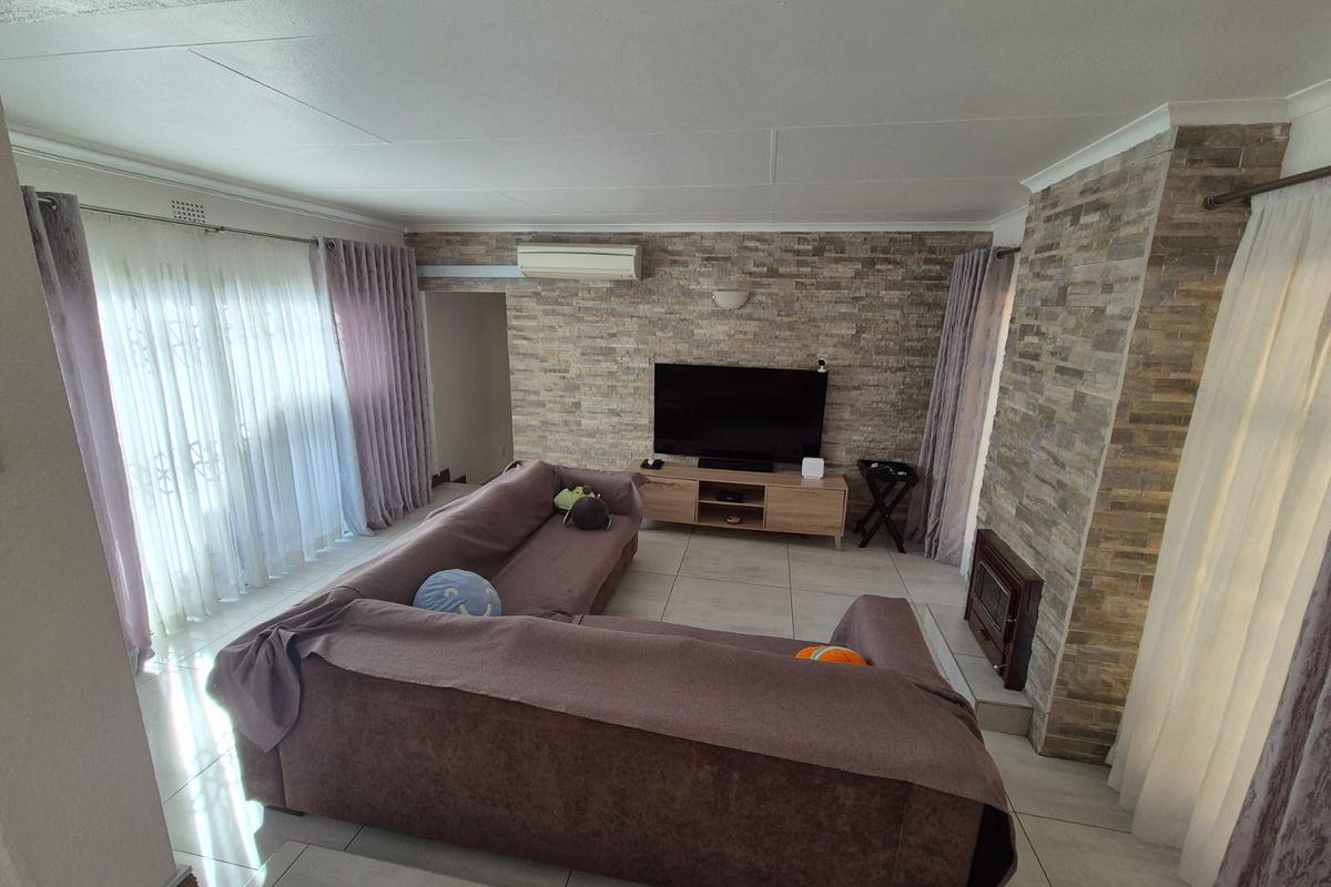Spacious living room featuring a stone-clad feature wall, built-in fireplace, and split-system air conditioning unit with large sliding doors leading to the exterior.