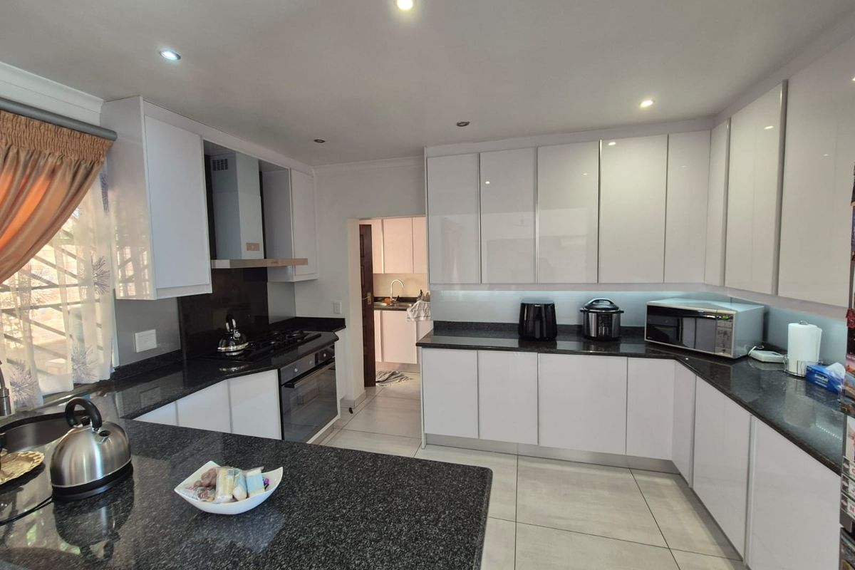 Modern kitchen featuring high-gloss white cabinetry, dark granite countertops, built-in oven, gas hob, and an integrated extractor fan, with an adjacent scullery area.