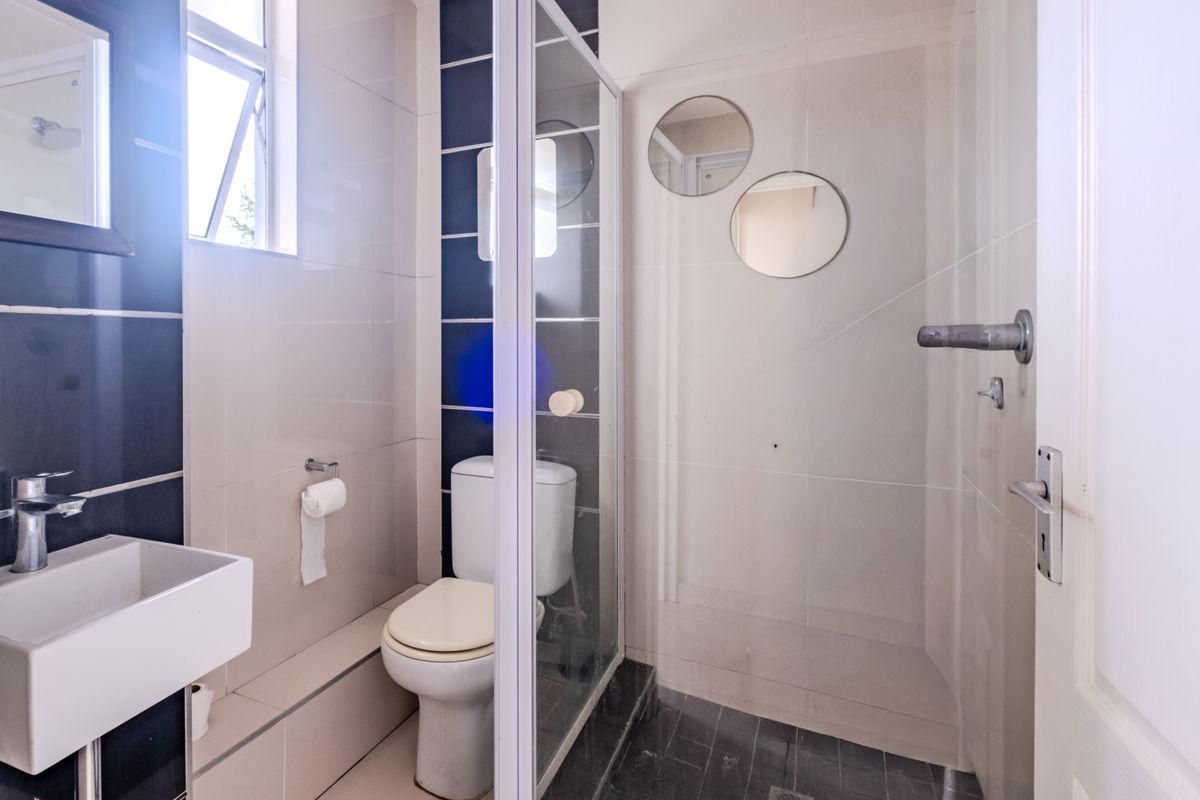 A compact bathroom featuring a wall-mounted basin, a toilet, and a glass-enclosed shower with tiled finishes and a small casement window.