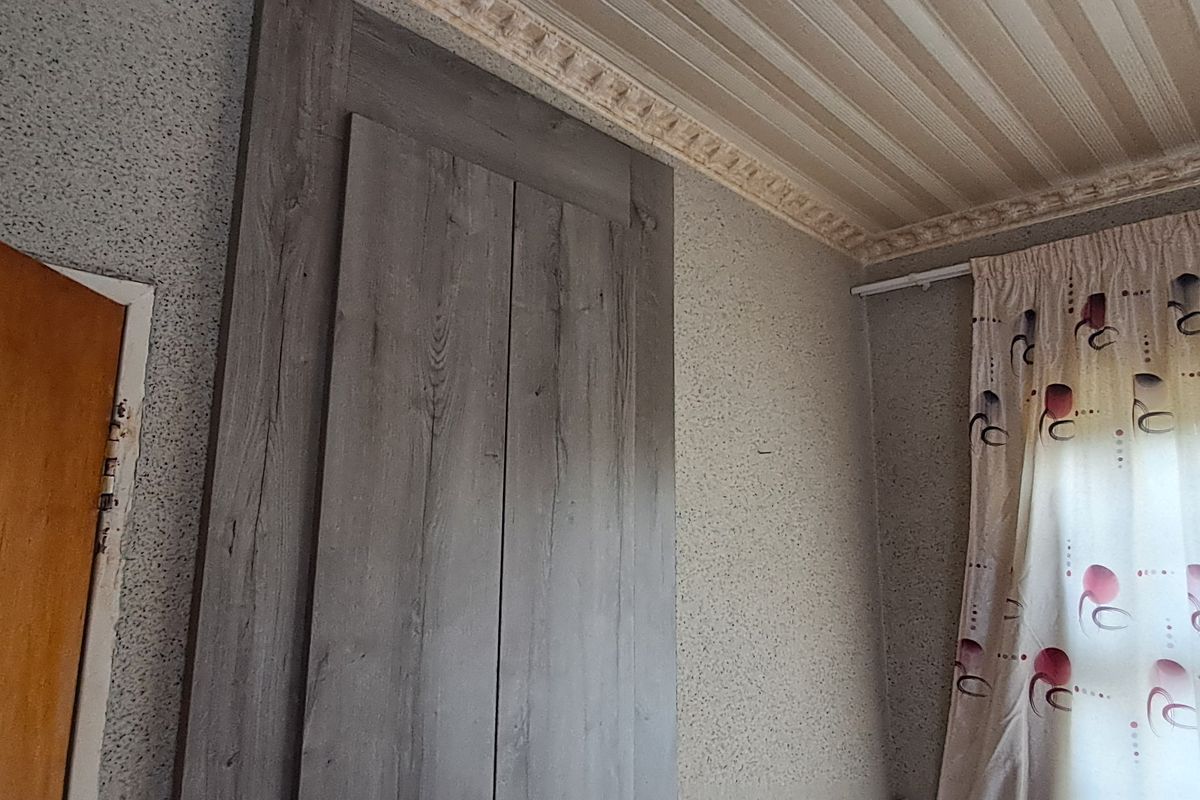 Bedroom interior featuring a built-in wardrobe, decorative ceiling cornice, and textured wallpaper finish.