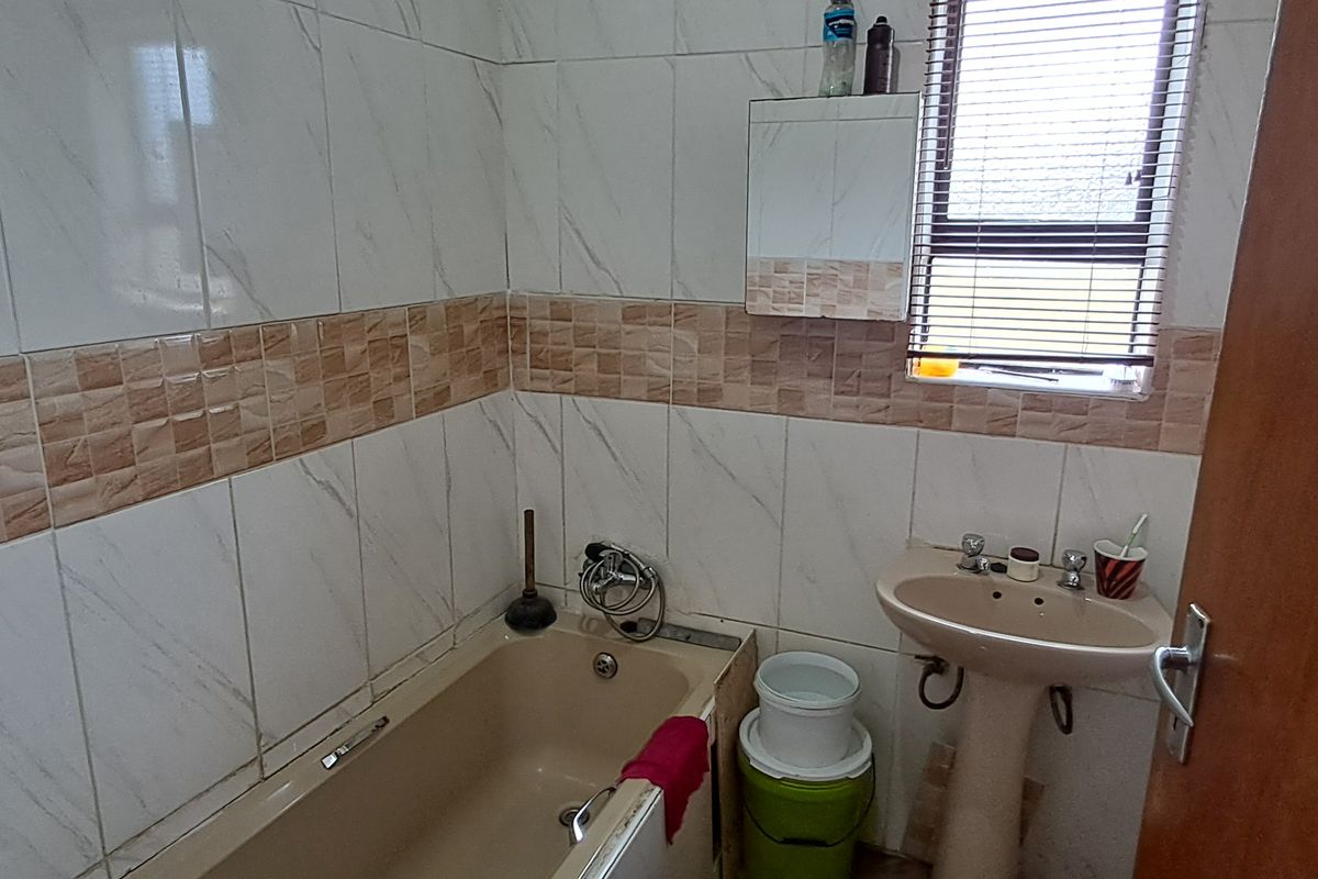 A compact bathroom featuring a bathtub, pedestal basin, and tiled walls with a window for natural light.