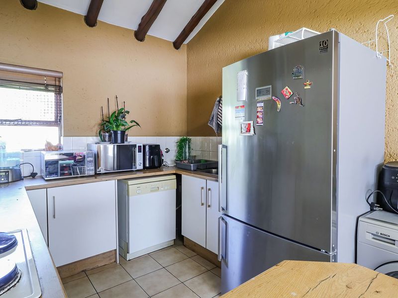 A functional kitchen featuring white cabinetry, laminate countertops, tiled backsplash, and exposed timber ceiling beams, providing a practical workspace with integrated appliance connections.