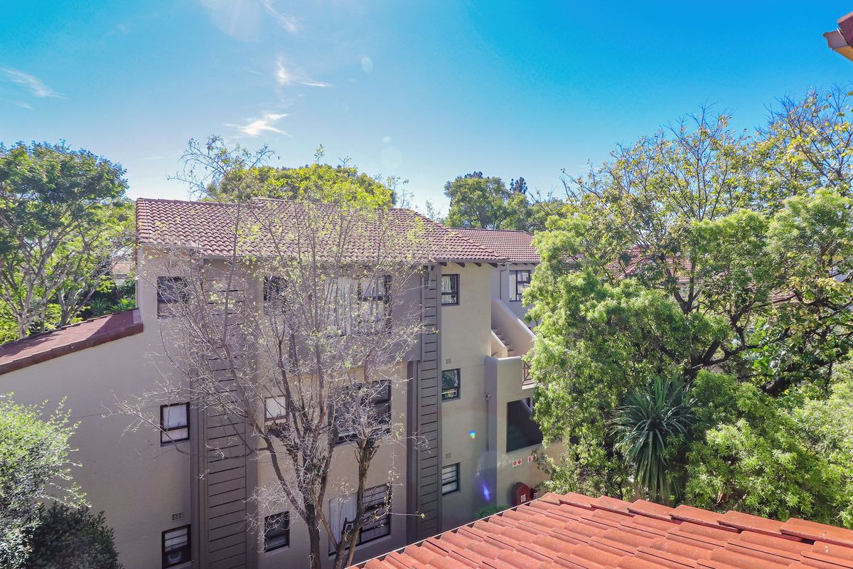 An elevated view of the apartment complex exterior, featuring tiled roofing, stucco walls, and mature surrounding trees.