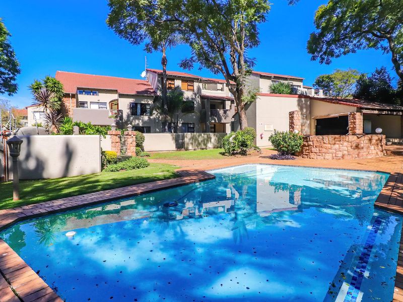 Communal swimming pool area featuring brick paving, stone-clad features, and established landscaping within an apartment complex setting.