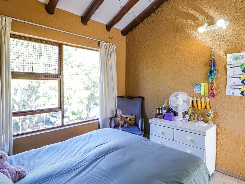 A bedroom featuring textured walls, exposed timber ceiling beams, and a large window providing natural light.