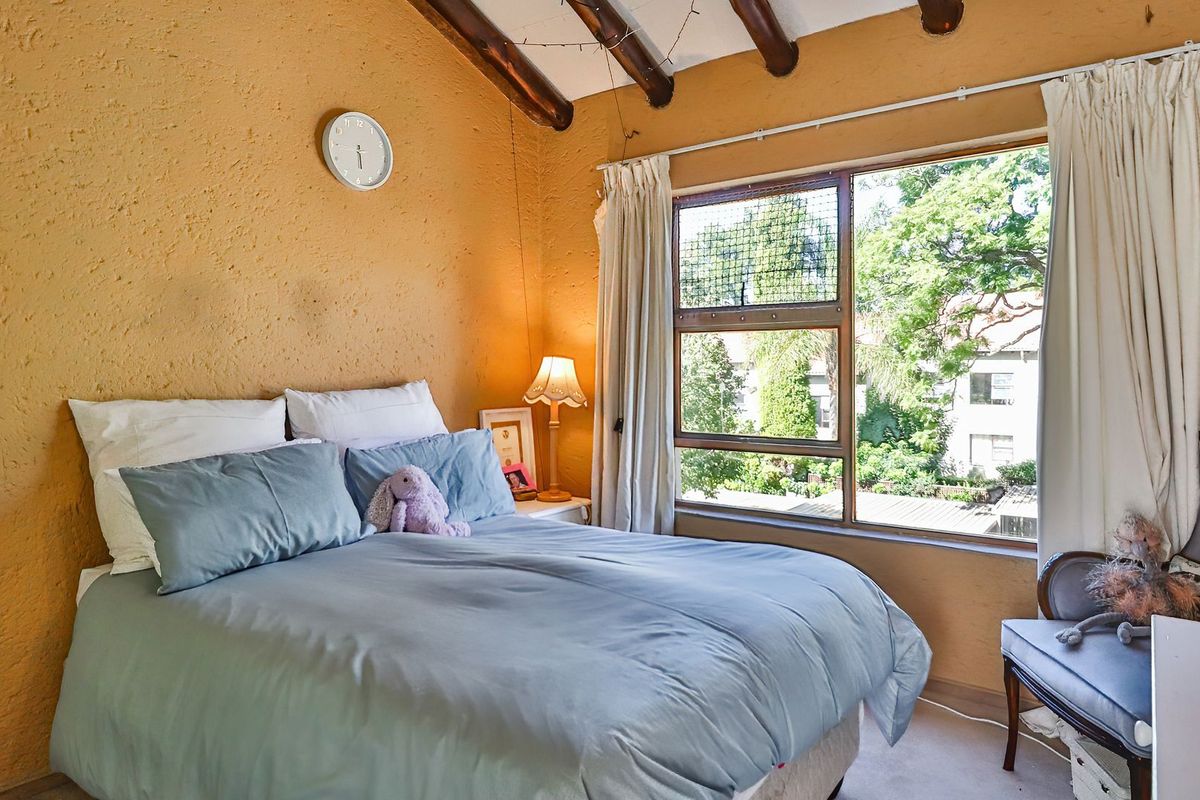 Cozy bedroom featuring exposed timber ceiling beams, textured walls, and a large window providing natural light and garden views.