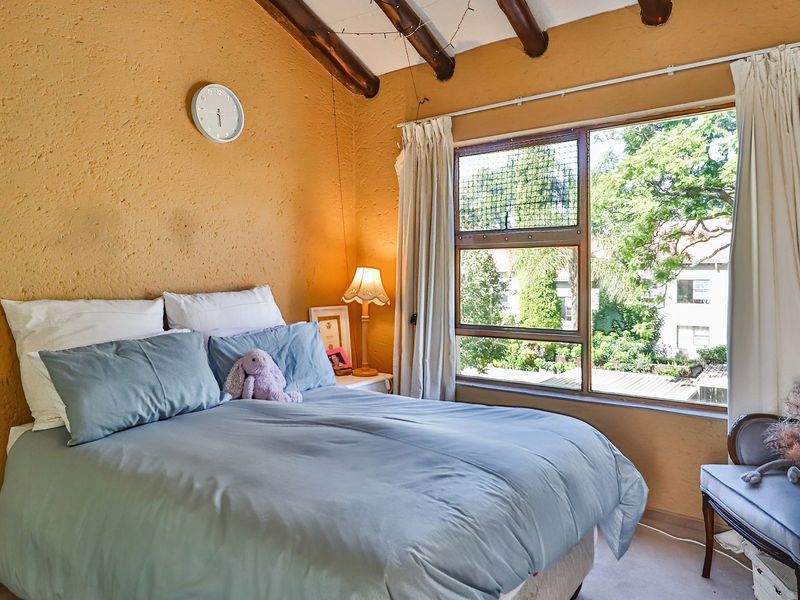 Cozy bedroom featuring exposed timber ceiling beams, textured walls, and a large window providing natural light and garden views.