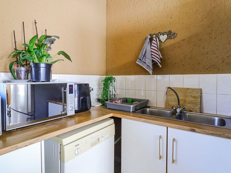 A functional kitchen corner featuring a double stainless steel sink, tiled splashback, wooden countertops, and white cabinetry.