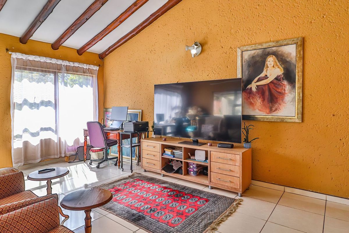 Living room featuring exposed timber ceiling beams, textured walls, and tiled flooring with access to an outdoor area via sliding glass doors.