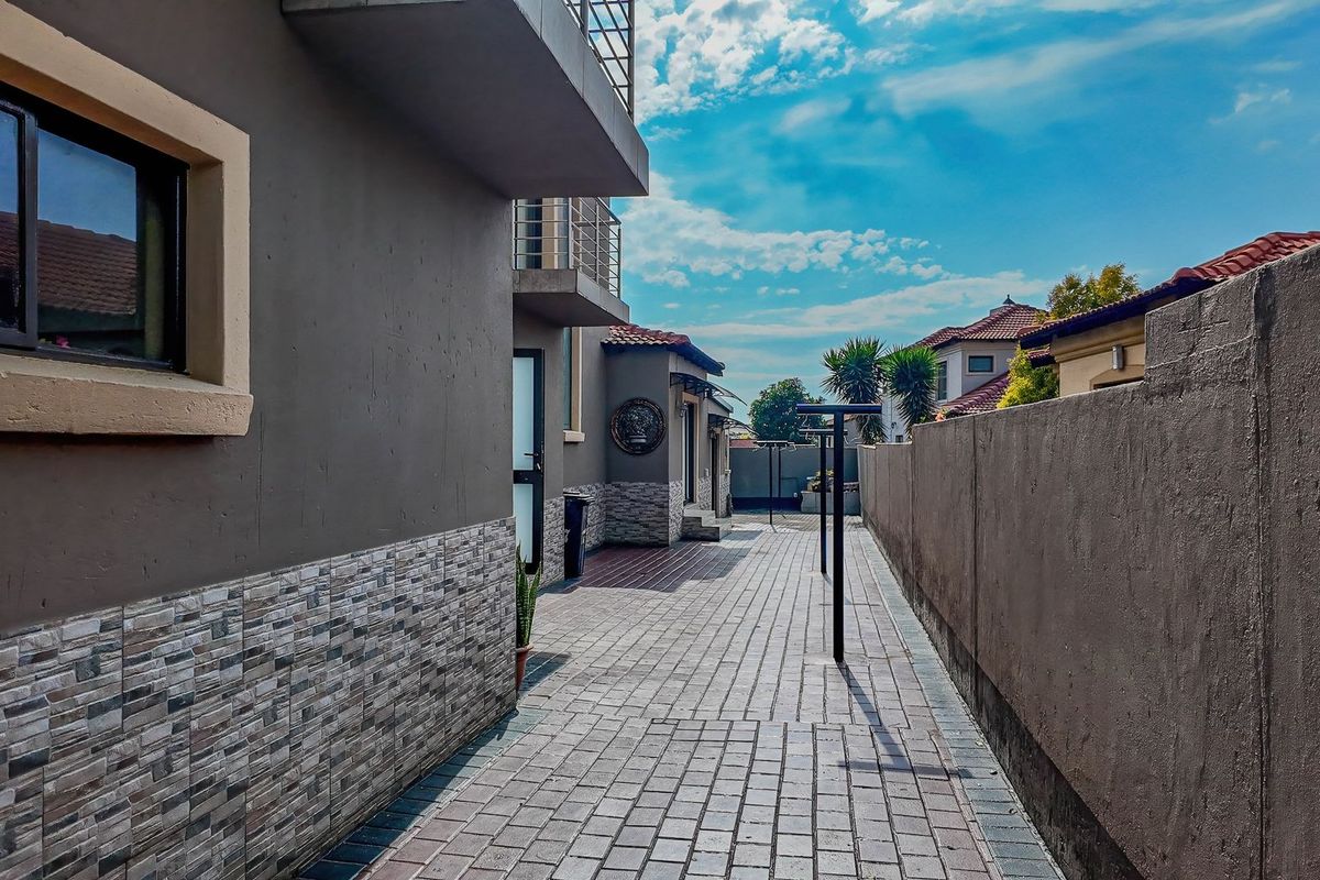 A paved side walkway leading to the rear of the property, featuring stone-clad exterior walls and a boundary wall.