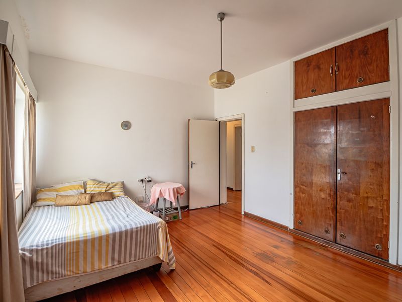 A bedroom featuring original hardwood flooring, built-in wooden cupboards, and a pendant light fixture, offering a classic foundation for renovation.