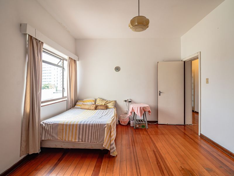 A bedroom featuring polished hardwood flooring, a large window providing natural light, and neutral wall finishes.