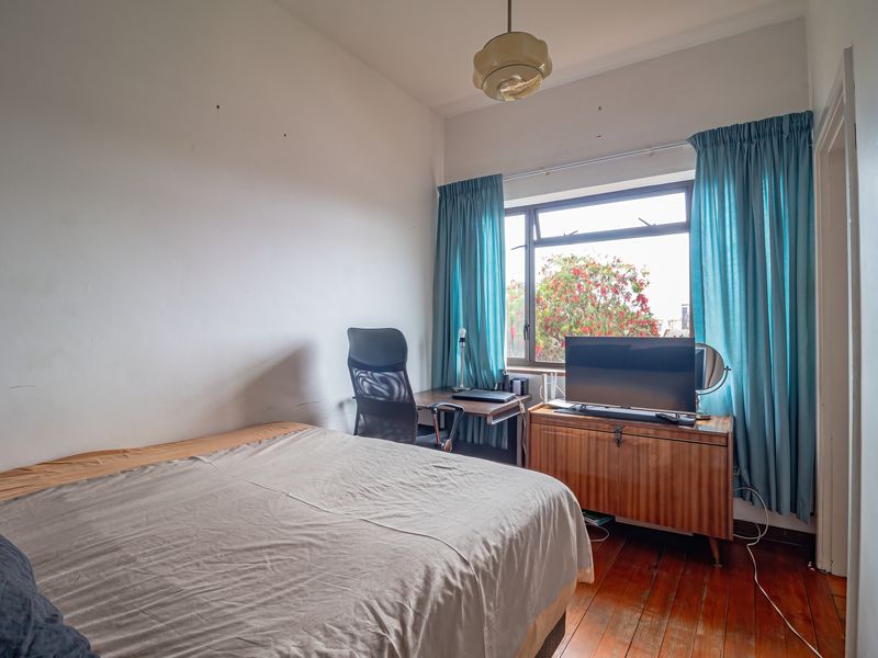 A bedroom featuring original hardwood flooring, a large casement window, and neutral wall finishes, offering a functional space with potential for modernization.