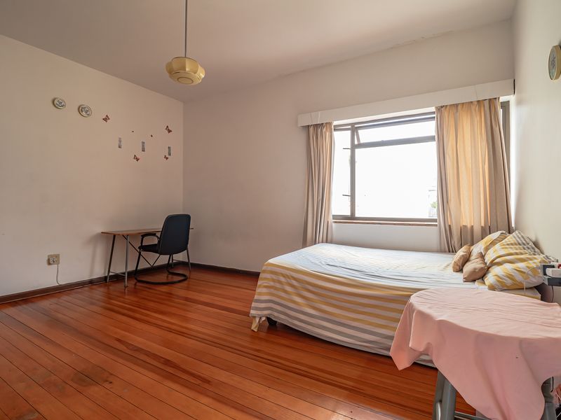A spacious bedroom featuring original hardwood flooring, large window with natural light, and neutral wall finishes, offering a blank canvas for renovation.