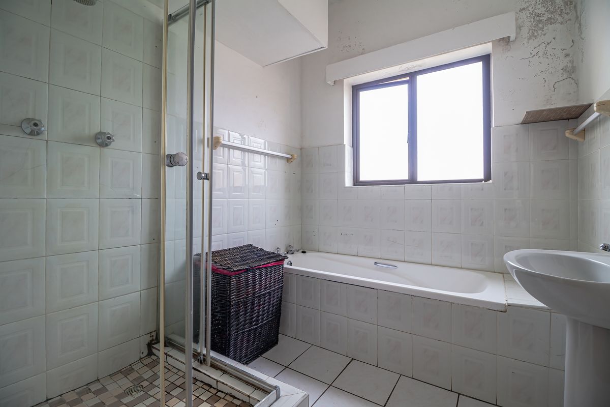 A dated bathroom featuring a shower enclosure, bathtub, and pedestal sink, requiring cosmetic updates and repairs to the wall and ceiling finishes.