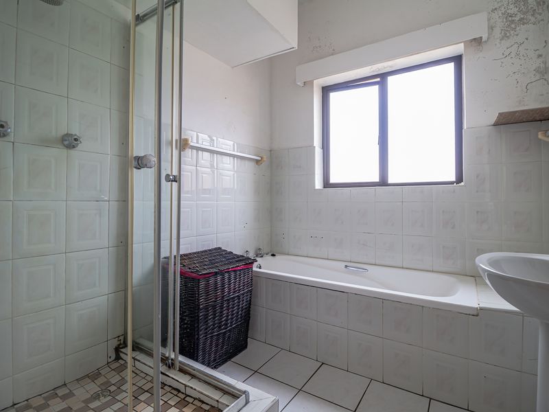 A dated bathroom featuring a shower enclosure, bathtub, and pedestal sink, requiring cosmetic updates and repairs to the wall and ceiling finishes.