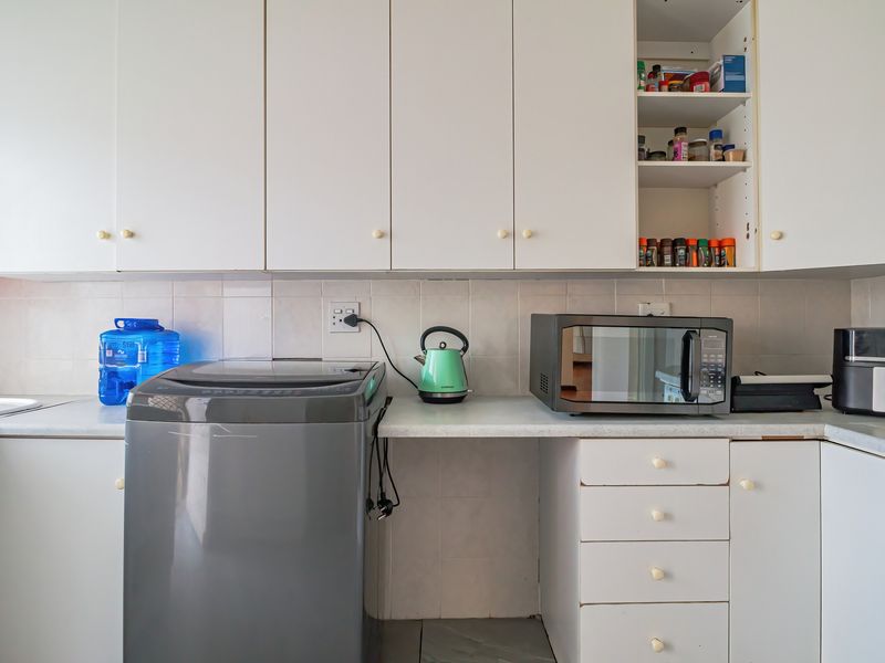A functional kitchen area featuring white built-in cabinetry, tiled backsplash, and laminate countertops with dedicated space for laundry appliances.