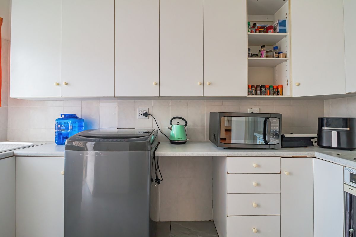 A functional kitchen area featuring white built-in cabinetry, tiled backsplash, and laminate countertops with dedicated space for laundry appliances.