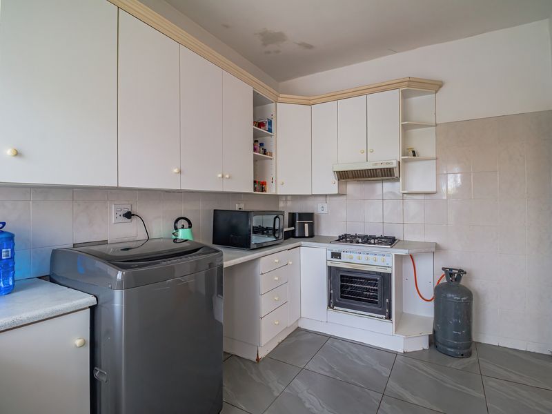A functional kitchen featuring white built-in cabinetry, a gas hob, an integrated oven, and tiled finishes, showing signs of wear and ceiling water damage.