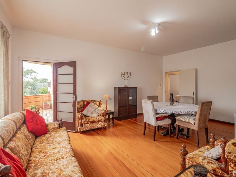 Open plan living and dining area featuring polished hardwood flooring and direct access to an outdoor balcony through a timber framed glass door.