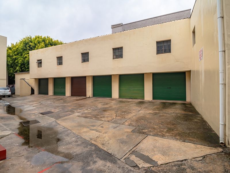 A row of multiple garage units with roller shutter doors and a shared concrete driveway area showing signs of wear and surface cracking.