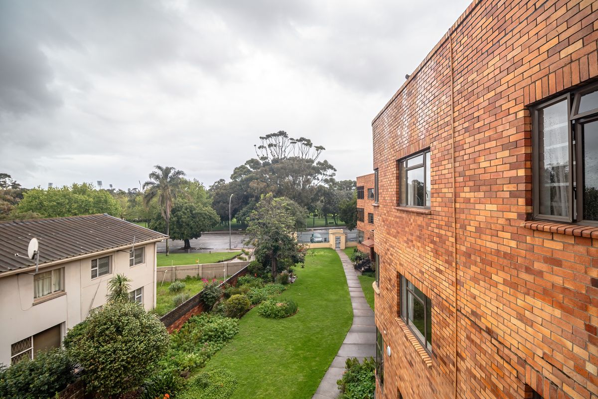 An elevated view of the apartment building's rear exterior, featuring a brick facade, paved walkway, and well-maintained communal garden area.
