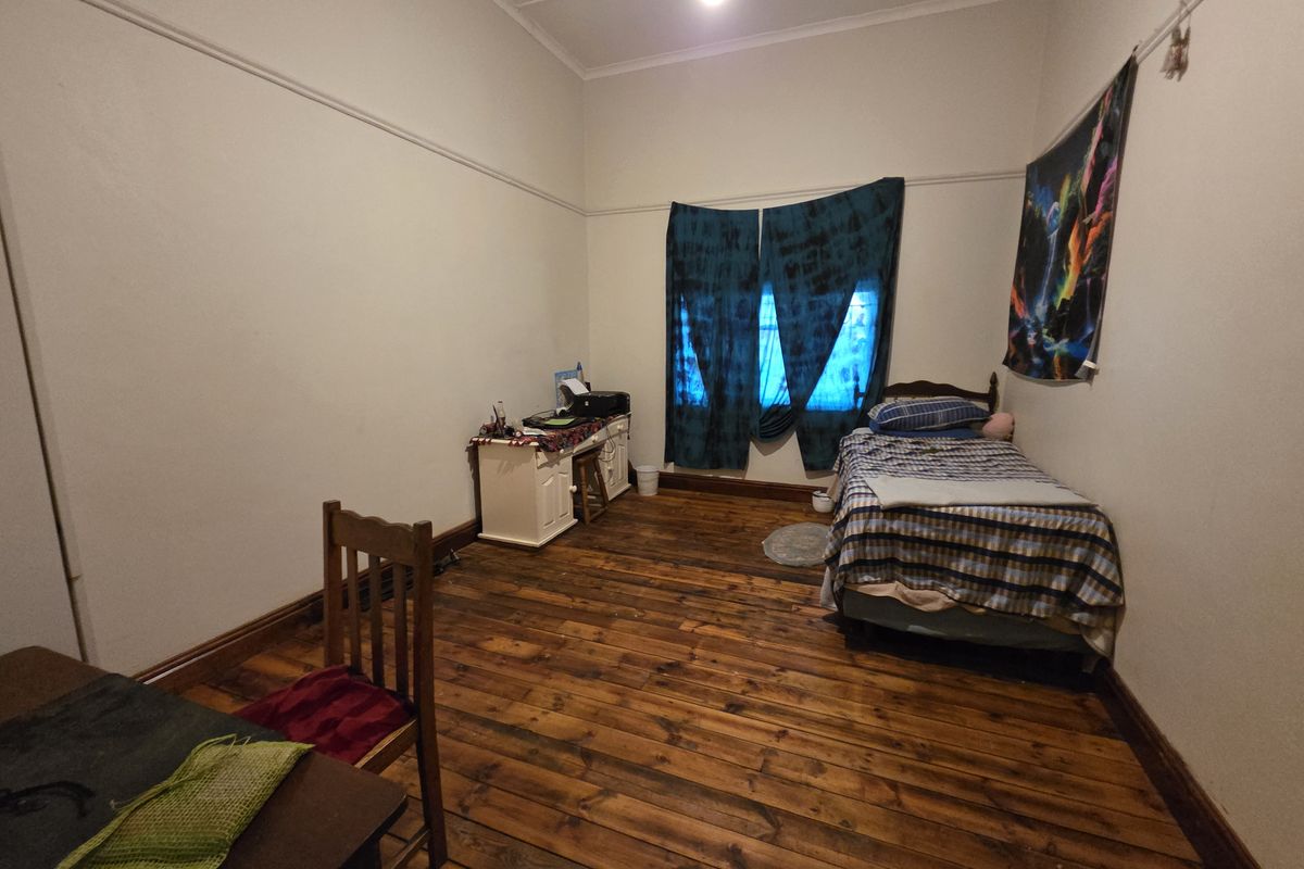 A bedroom featuring original timber flooring, high ceilings with picture rails, and a window with natural light.