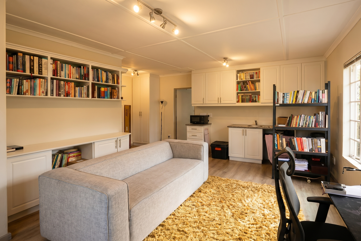 A well-lit living room featuring extensive built-in cabinetry and shelving, laminate flooring, and large windows providing natural light.